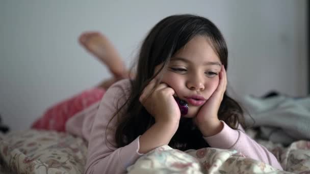一个无聊的小女孩感到极度无聊 无事可做 双手托着下巴躺在床上 忧心忡忡的8岁儿童近视脸 — 图库视频影像