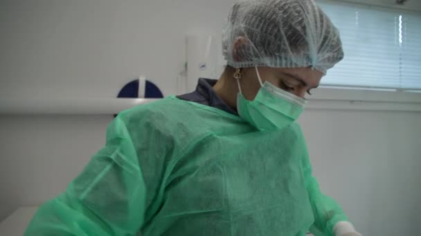 女性歯科医は 臨床的鎮静剤の制服を着用する準備をしています エプロン マスク ヘッドギアを着用している女性 — ストック動画