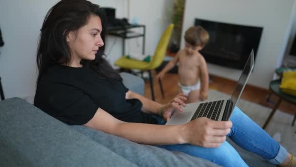 Mor Sitter Soffan Och Använder Laptop Med Bebisbarn Föräldrars Multitasking — Stockvideo