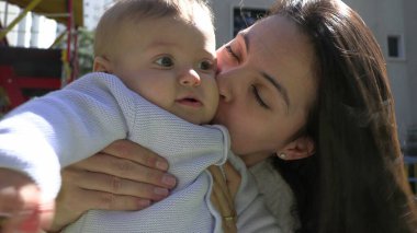 Otantik anne ve bebek dışarıda sarılıp öpüşüyor.