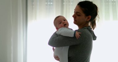 Real life authentic mom kissing and consoling crying infant baby