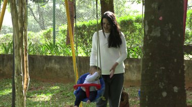 Samimi anne, bebeği parkta salıncakta sallıyor.