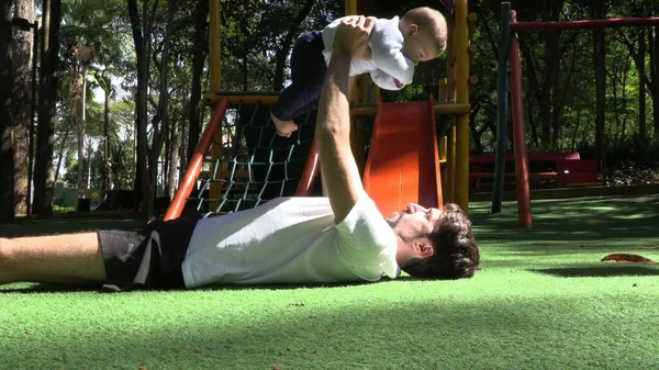 Father lifting baby son in the air at park casual father lifting infant upwards in the air at playground