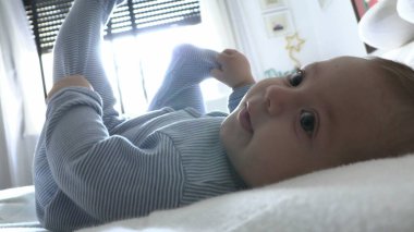 Tatlı, tatlı bebek yatakta uzanmış kameraya bakıyor.