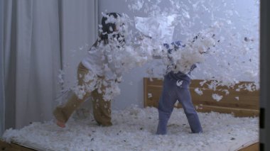 Çocuklar yastık savaşında eğleniyor. Tüyler havada uçuyor. Kız kardeş hız rampasında küçük kardeşle dövüşüyor.