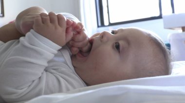 Sevimli bebek ayağını ağzına sokup mutlu ve neşeli bir şekilde kalkıyor.