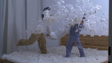 Çocuklar yastık savaşında eğleniyor. Tüyler havada uçuyor. Kız kardeş hız rampasında küçük kardeşle dövüşüyor.