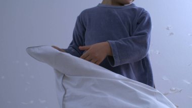 Çocuklar yastık savaşı oynuyorlar. Çok yavaş çekimde yatakta duruyorlar. Tüyleri uçuşan 1000 fp.