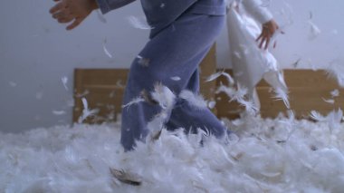 Çocuklar yastık savaşı oynuyorlar. Çok yavaş çekimde yatakta duruyorlar. Tüyleri uçuşan 1000 fp.