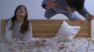 Küçük kardeşin yatağa atladığı mutlu bir an. Kız kardeşi gülerken mutlu bir aile hayatı. Süper yavaş çekimde 1.000 fp.