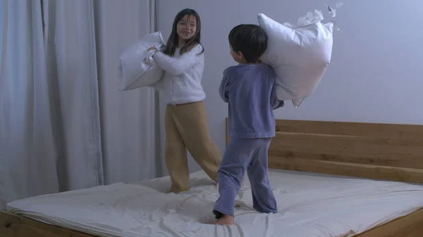 Children engaged in pillow fight with feathers flying everywhere in the air captured in super slow motion at 1000 fps with a high speed camera while standing on bed