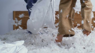 Çocuklar yastık savaşının ortasında yatakta zıplayarak havada uçuşan tüylerle yüksek hızlı bir kamerayla yakalanırlar.