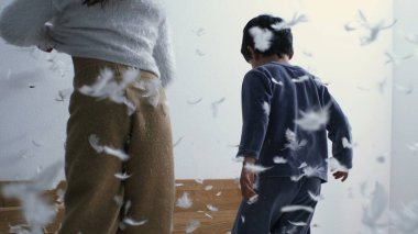 Arka plandaki çocuklar yatakta zıplarken havadan tüy düşüyor.