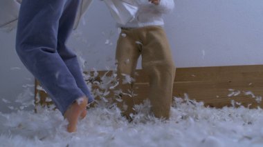 Çocuklar yastık savaşının ortasında yatakta zıplayarak havada uçuşan tüylerle yüksek hızlı bir kamerayla yakalanırlar.