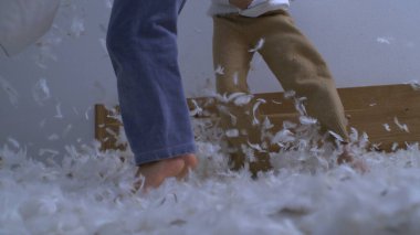 Çocuklar yastık savaşının ortasında yatakta zıplayarak havada uçuşan tüylerle yüksek hızlı bir kamerayla yakalanırlar.