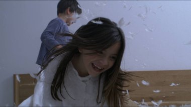 Çocuklar yastık savaşının ortasında havaya tüy atıyorlar. Kardeşler tüylerle çevrili kaygısız bir an yaşarlar.