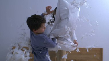 Mutlu kardeşler yastık savaşıyla eğleniyor, havada uçuşan tüyler, kaygısız neşeli oyunlar oynayan çocuklar süper yavaş çekimde yakalandı.