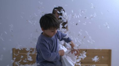 Mutlu kardeşler yastık savaşıyla eğleniyor, havada uçuşan tüyler, kaygısız neşeli oyunlar oynayan çocuklar süper yavaş çekimde yakalandı.