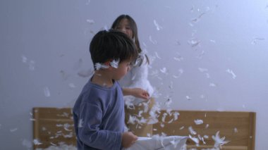 Mutlu kardeşler yastık savaşıyla eğleniyor, havada uçuşan tüyler, kaygısız neşeli oyunlar oynayan çocuklar süper yavaş çekimde yakalandı.