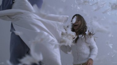 Kardeşler yatakta zıplarken yastık savaşı yapıyorlar. Süper yavaş çekimde havada uçuşan tüylü 1000 fps 'de yakalandılar. Mutlu çocukluk duyguları.