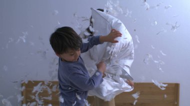 Mutlu kardeşler yastık savaşıyla eğleniyor, havada uçuşan tüyler, kaygısız neşeli oyunlar oynayan çocuklar süper yavaş çekimde yakalandı.