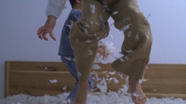Yatakta zıplayan neşeli çocuklar yüksek hızlı kamerayla 1000 fps hızla çekiliyorlar. Tüylerle kaplı küçük kız hoplayıp zıplarken