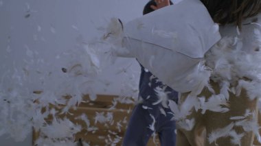 Yastık Savaşındaki Çocukların Eğlenceli Aktivitesi, Tüyler Süper Yavaş Hareket 'te uçuyor, küçük kardeş yatak odasında kız kardeşinin yanına yastık atıyor.