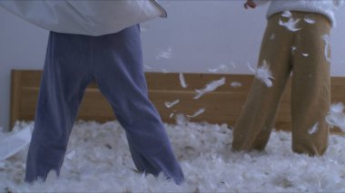 Çocuklar yastık savaşının ortasında yataklarında tüyleri uçuşan ve hız rampasında 1000 fp hızla çekilen bir kamerayla yakalanan çocuklar.