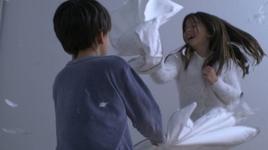 Kardeşler yatakta zıplarken yastık savaşı yapıyorlar. Süper yavaş çekimde havada uçuşan tüylü 1000 fps 'de yakalandılar. Mutlu çocukluk duyguları.