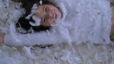 Yatağa düşen mutlu küçük kız, havada uçuşan binlerce tüyle birlikte, 1000 fps hızında yüksek hızlı bir kamerayla yakalandı. Tüylerin arasında gülümseyen çocuk
