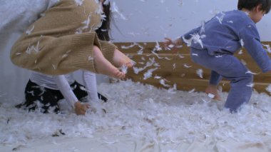 Tüylerle kaplı çocukların yatakta zıplayıp mutlu bir aile anını süper yavaş çekimde 1000 Fps 'te yakalıyorlar. Kızlar yatağa atlarken, anneler havaya kuş tüyü fırlatıyor.