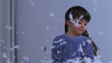 Çocuklar yastık kavgasının ortasında eğleniyor, küçük kardeş oyun sırasında tüylerle kaplı.