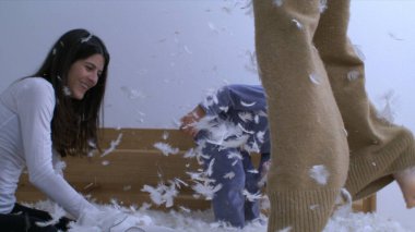 Anne ve çocuklar yatak odasında yavaş çekimde oynarken tüyler uçuşuyor. Anne ve çocuklar yastık savaşı yapıyor. Gerçek mutluluk.