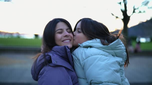 幸せな娘は頬に母親にキスし 暖かい抱擁を与えています 公園で寒い季節にコートを着ている8歳の子供と30代の女性の肖像画 — ストック動画