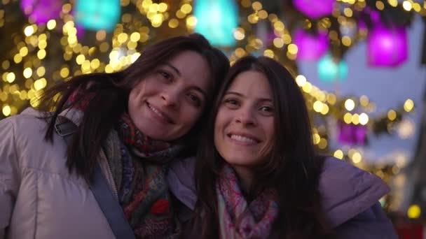 2人の姉妹の肖像画は 夜の背景に電球を当ててカメラで微笑んで顔を閉じました コートとスカーフを着ている女性 — ストック動画