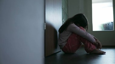 Zorlanan çocuk koridorda oturuyor yüzünü kapatıyor zor zamanlarda yalnızlık ve yalnızlık hissediyor. Çocukluk depresyonu