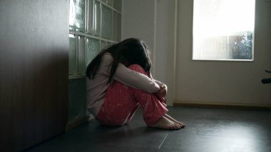 Depresyondan muzdarip üzgün bir çocuk koridorda tek başına oturmuş yalnızlık hissediyor. Korkmuş, korkmuş, çocukluğunda mücadele eden yüzü örten küçük bir kız.