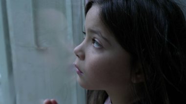 Üzgün, düşünceli çocuk camdan dışarı bakıyor ve kendini evde kapana kısılmış hissediyor. Yalnızlık çeken küçük bir kız