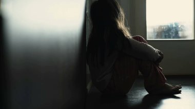 Üzgün, depresif, utançla kaplı, çocukluğunda akıl hastalıklarıyla boğuşan bir çocuk silueti. Evinin koridorunda kasvetli bir sahnede oturan küçük kız.