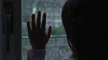 Evdeki cam pencereye yaslanmış, çocukluk yalnızlığı ve yalnızlığı tasvir eden çocuk eli.