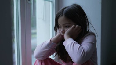 Üzgün, düşünceli, küçük bir kız. Pencerenin kenarında yalnızlık hissedip düşünceli bakışlarla manzaraya bakıyor. Derin düşüncelere dalmış çocuk