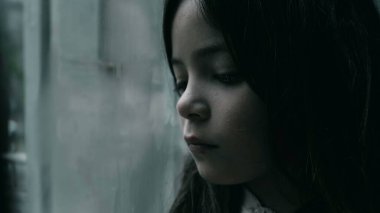 Üzgün ve yalnız hisseden bir çocuk cama yaslanıyor. Çocukluğunda depresyonla boğuşan küçük bir kızın yakın plan yüzü.