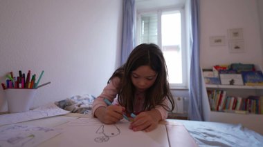 Yatak odasında kağıda resim çizen konsantre küçük kız, kalem kullanan çocuk. Sanatsal çocukluk gelişimi, boş zaman