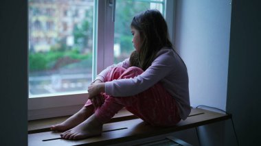 Pencere kenarındaki Bunalımlı Küçük Kız, Çocuklukta Endişe ve Endişe. Evde kendini yalnız hisseden çocuk zorluklarla boğuşuyor.