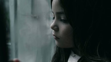 Üzgün ve yalnız hisseden bir çocuk cama yaslanıyor. Çocukluğunda depresyonla boğuşan küçük bir kızın yakın plan yüzü.