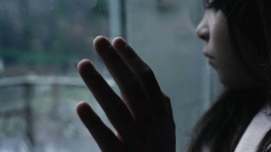 Depresyon ve değersizlikle boğuşan küçük bir kızın çocukluk hastalığının tasviri. Camlara yaslanmış kasvetli manzaraya bakıyor.