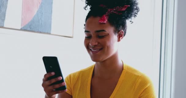 ハッピー ヤング アフリカ系アメリカ人女性が自宅で笑顔で携帯電話機にポジティブな通知メッセージを受け取りました 携帯電話の画面を見ている黒人の大人の少女 — ストック動画