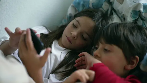 Young Siblings Sharing Cellphone Screen in Bed, Sister and Brother Looking at Smartphone Together