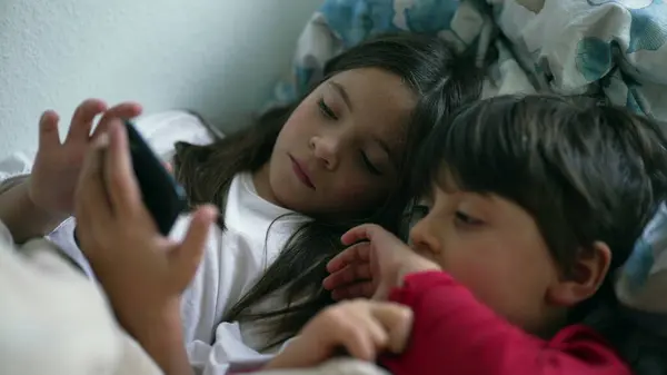 Young Siblings Sharing Cellphone Screen in Bed, Sister and Brother Looking at Smartphone Together