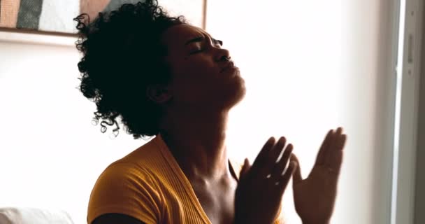 ある宗教的な若い黒人女性は 目を閉じて神からの助けとサポートを求めて静かに家で祈り 空を感じる信仰と精神を指差しています — ストック動画